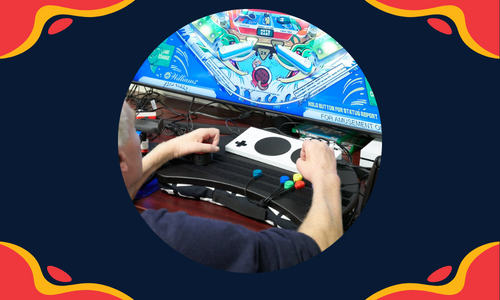 A graphic with red and yellow blobs in all 4 corners of the rectangle with a circular photo in the center of a behind the back shot of a person with a disbaility playing a game. Showing their hands on a laptray with various assistive tech for gaming.