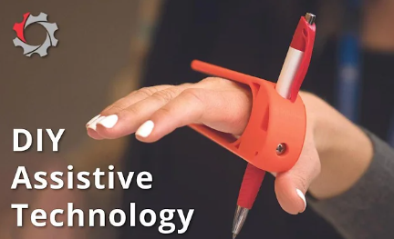 A screenshot from a video with DIY Assistive Technology written in the bottom left and a hand using a Pen Holder assistive device.